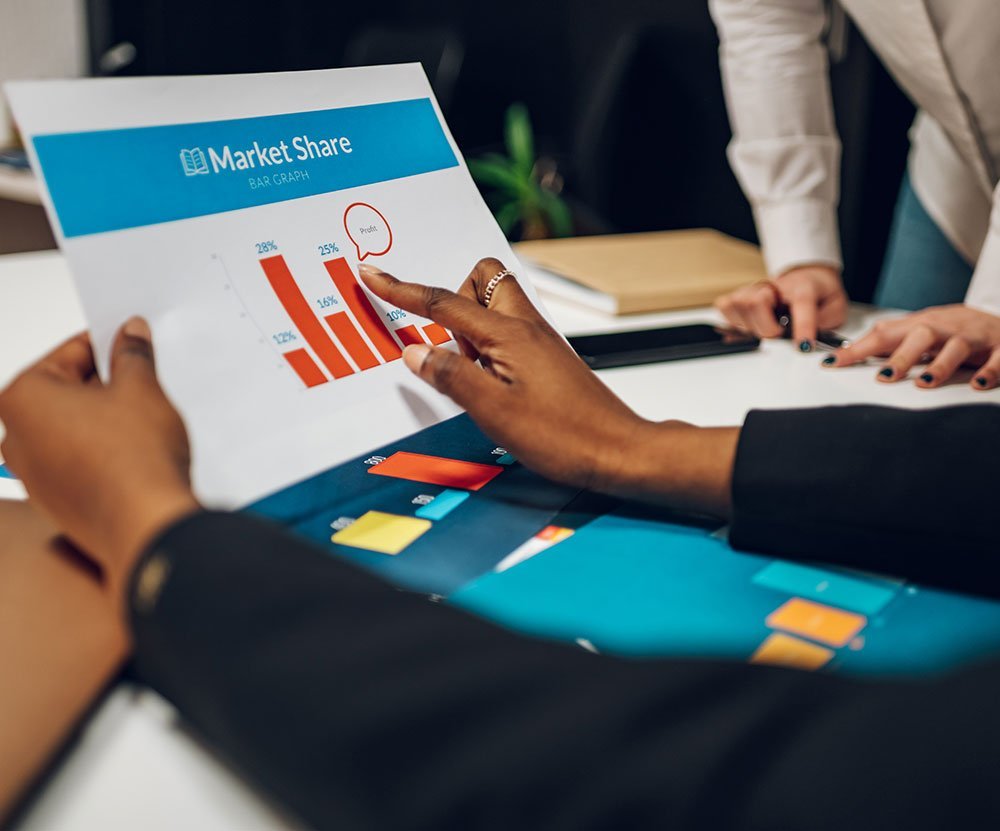 Professionals discussing a market share bar graph during a business meeting.