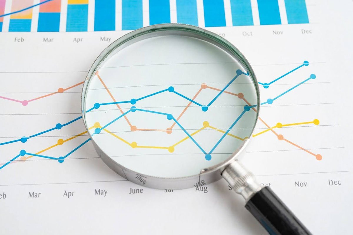 Magnifying glass analyzing a line graph with multiple colored trend lines on paper.