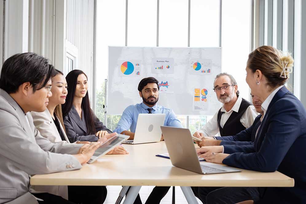 Business team engaged in a strategic meeting with charts and analytics displayed on the board in a bright office.