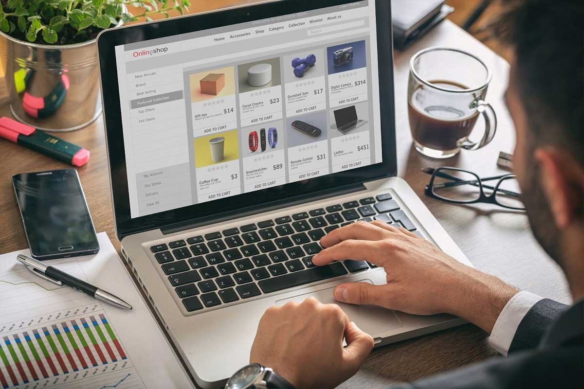 Man shopping online on his laptop, with a cup of coffee and smartphone nearby.