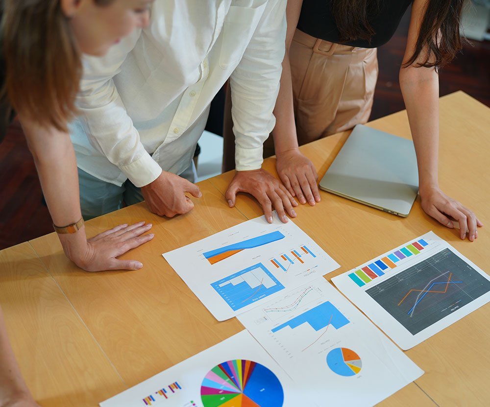 Three professionals analyzing financial charts and graphs on a table during a team meeting.