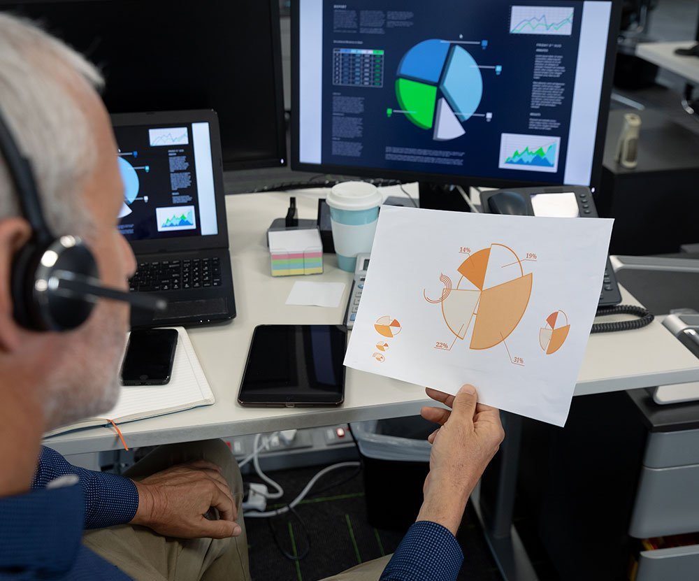 Senior analyst reviewing pie chart at a multi-screen data analysis workstation.