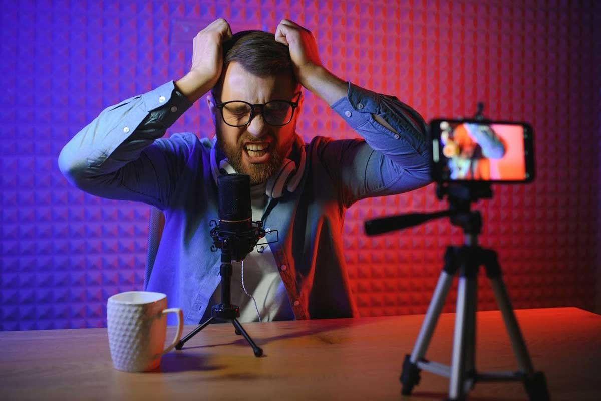 Man with glasses looking stressed while recording a video in a studio with colorful background.