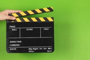 Hand holding a film clapperboard against a green background.