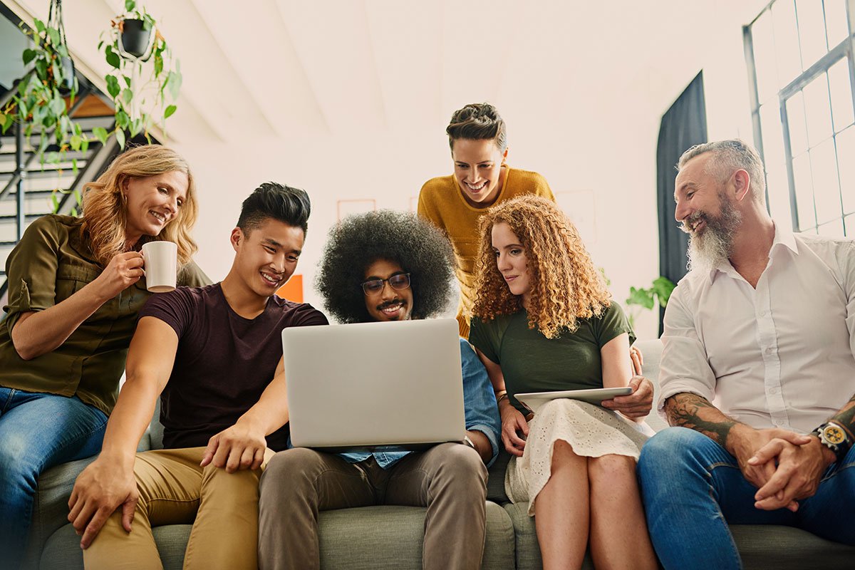 A group of people sitting together on a couch, happily gathered around a laptop, enjoying a shared moment.